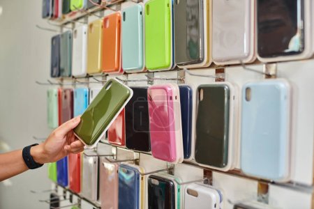cropped view of man near showcase with various colorful phone cases in private shop, small business