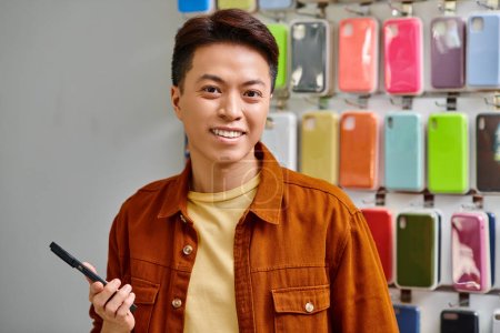 happy asian business holding smartphone and at camera in private electronics shop, small business