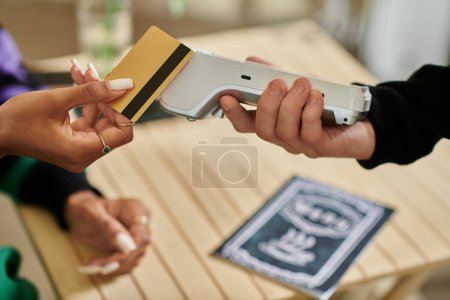 cliente femenino que sostiene la tarjeta de crédito cerca del lector de tarjetas, mano recortada en la mujer que paga en la cafetería vegana