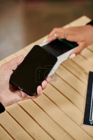Téléchargez les photos : Paiement par smartphone, vue recadrée de l'homme tenant son smartphone près du lecteur de carte dans un café végétalien - en image libre de droit