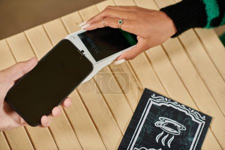 pago del teléfono móvil, vista recortada de la mujer sosteniendo su teléfono inteligente cerca del lector de tarjetas en la cafetería vegana