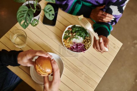 vista superior de la joven y diversa pareja disfrutando de comida vegana en la cafetería, hamburguesa con tofu y ensalada