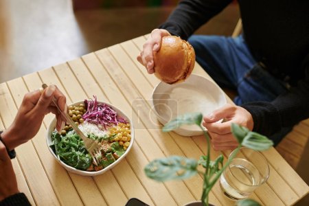 top view of young and diverse couple enjoying vegan meal in cafe, burger with tofu and salad bowl