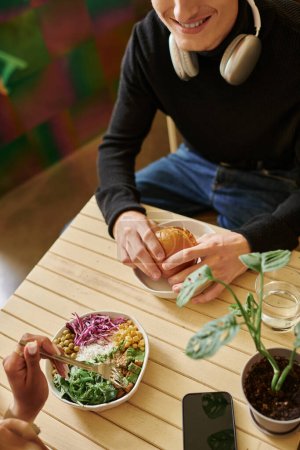 overhead view of young diverse couple enjoying vegan meal in cafe, burger with tofu and salad bowl