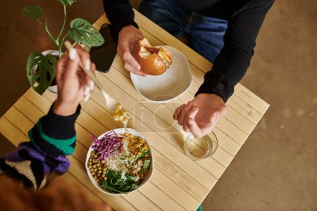 cropped shot of man and woman eating vegan tofu burger and salad bowl in vegan cafe, vegetarian