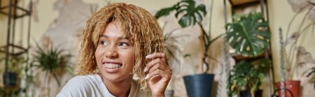 bannière de joyeux afro-américaine jeune femme avec bretelles souriant dans un café végétalien avec des plantes