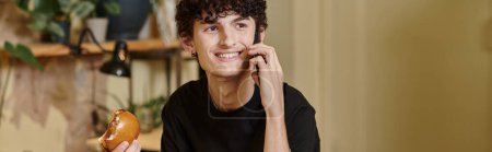 happy and young man holding plant-based tofu burger and talking on smartphone in vegan cafe, banner