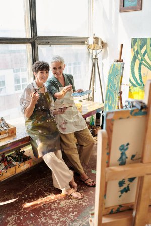 souriant mature femmes artistes pointant vers chevalet avec atelier d'artisanat au pinceau, passe-temps créatif