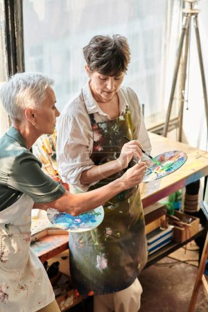reife Künstlerinnen beim Mischen von Farben auf Palette während eines Meisterkurses im Kunstatelier, kreatives Hobby