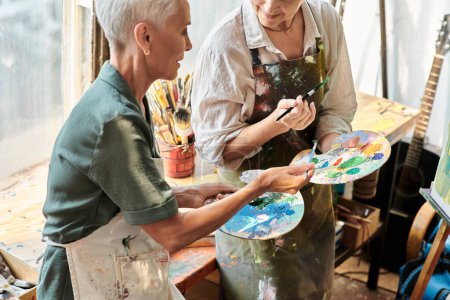 reife Malerinnen beim Mischen von Farben auf Palette bei Meisterkurs in Handwerkswerkstatt, Hobby