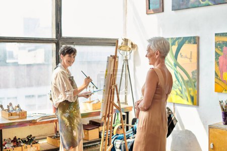 Téléchargez les photos : Heureuse femme mûre peinture élégante amie féminine posant dans l'atelier d'art, processus artistique - en image libre de droit