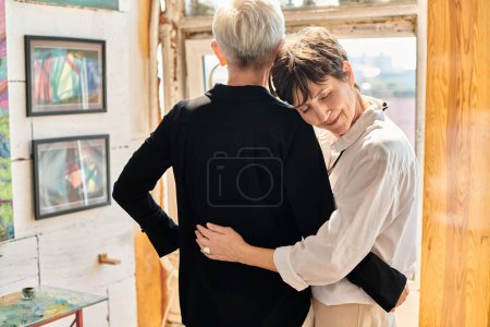 Photo for Happy mature woman with closed eyes embracing stylish lesbian partner  in contemporary art studio - Royalty Free Image