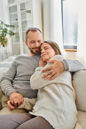 happy child-free couple with closed eyes embracing on cozy couch in living room, calm lifestyle