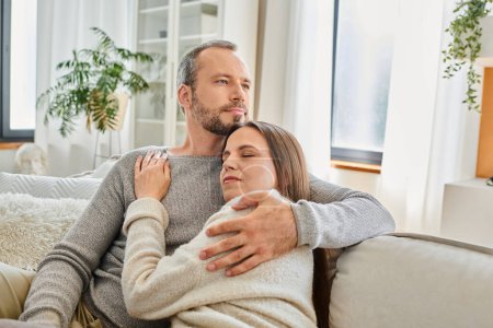 pleased child-free couple embracing on cozy couch in modern living room, calm lifestyle and serenity