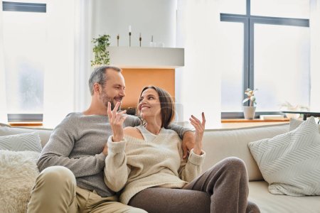esposa alegre hablando con el marido sonriente en el sofá acogedor en la sala de estar, moderno estilo de vida libre de niños