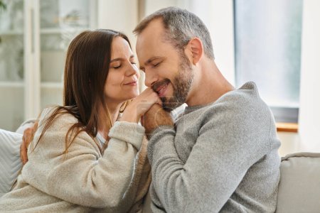 glücklicher Mann mit geschlossenen Augen, der die Hände seiner entzückten Frau im Wohnzimmer küsst, Liebe und Zärtlichkeit