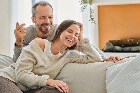 excited child-free couple laughing on couch in modern cozy living room, relaxation and fun at home