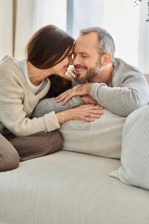 delighted child-free couple smiling face to face in cozy living room at home, unity and harmony