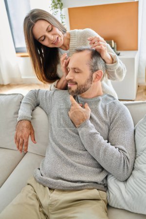 smiling wife touching head of pleased husband sitting on couch with closed eyes, child-free couple