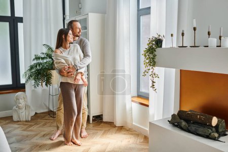happy child-free couple standing at window in cozy  living room with modern interior and fireplace