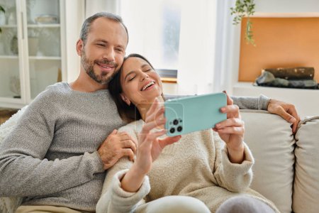 relaxed and happy child-free couple browsing social media on mobile phone at home, quality time