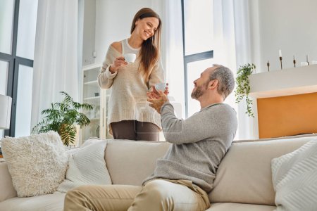 happy child-free couple holding coffee cups in modern living room of cozy apartment, serenity
