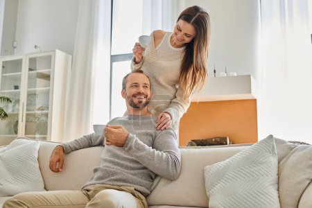 cheerful child-free couple holding morning coffee in modern living room of cozy apartment, serenity
