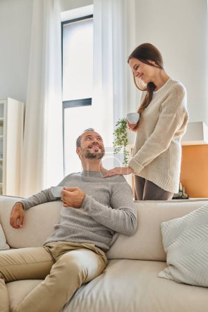 child-free couple with coffee cups smiling at each other in cozy living room at home, happy morning