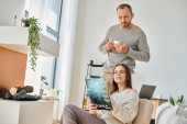 interested woman reading science magazine near husband with coffee cup on couch, child-free couple Tank Top #689854506