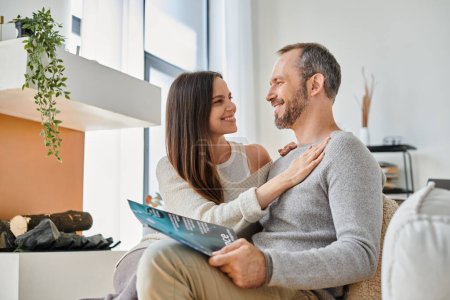 smiling woman embracing husband reading science magazine on couch at home, child-free life