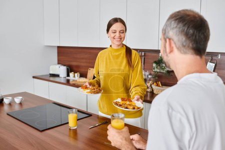 Photo for Joyful wife holding delicious breakfast near husband with orange juice in kitchen, child-free couple - Royalty Free Image