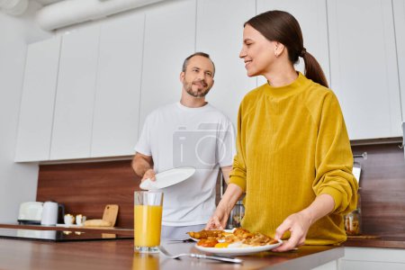 Téléchargez les photos : Couple sans enfant servant un délicieux petit déjeuner dans la cuisine moderne ensemble, la sérénité et l'harmonie - en image libre de droit