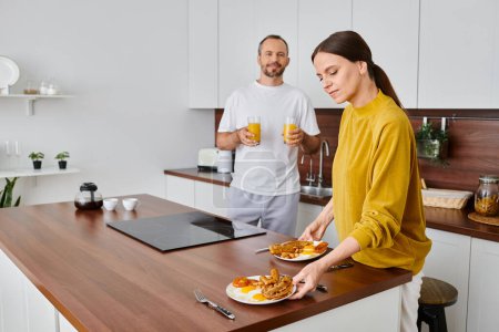 Téléchargez les photos : Homme tenant du jus d'orange près d'une femme attentionnée servant un délicieux petit déjeuner dans la cuisine, vie sans enfant - en image libre de droit