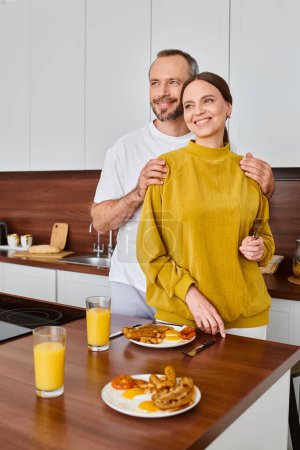 smiling man hugging shoulders of wife near delicious breakfast in kitchen, child-free couple