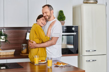 Téléchargez les photos : Sourire couple sans enfant embrassant près de délicieux petit déjeuner dans la cuisine moderne, l'amour et les soins - en image libre de droit