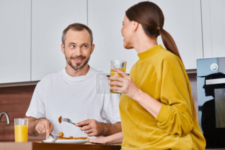 Téléchargez les photos : Homme souriant ayant délicieux petit déjeuner près de la femme avec du jus d'orange dans la cuisine, mode de vie sans enfant - en image libre de droit