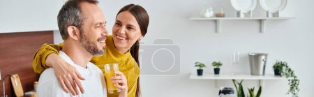 caring wife holding fresh homemade orange juice near delighted husband in kitchen, banner