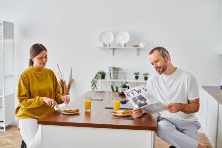 Téléchargez les photos : Homme positif lisant les nouvelles d'affaires près de la femme appréciant le petit déjeuner savoureux dans la cuisine, bannière horizontale - en image libre de droit