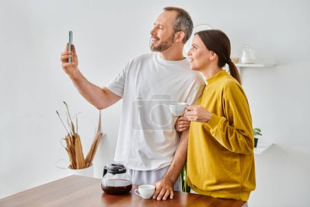 glücklicher Mann beim Selfie mit lächelnder Frau und morgendlichem Kaffee in der Küche, kinderfreier Lebensstil