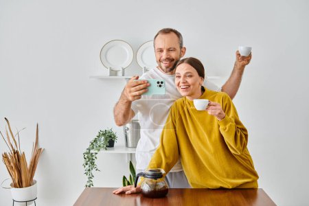 excitada pareja libre de niños hablando autorretrato en el teléfono inteligente durante el café de la mañana en la cocina