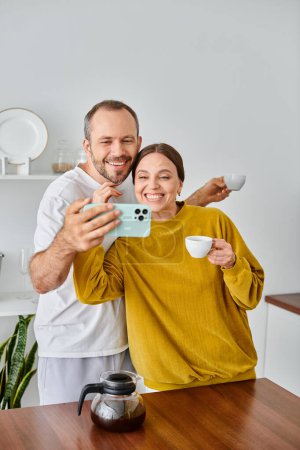 fröhliches kinderfreies Paar, das beim Morgenkaffee in der Küche Selbstporträt auf dem Smartphone spricht