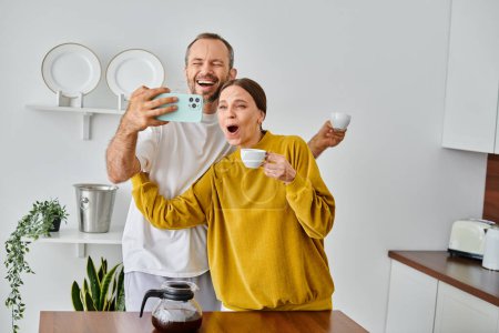 happy child-free couple having fun and  taking selfie during morning coffee in modern kitchen