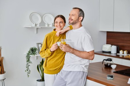 sonriente pareja sin niños con café aromático y jugo de naranja fresco mirando hacia otro lado en la cocina