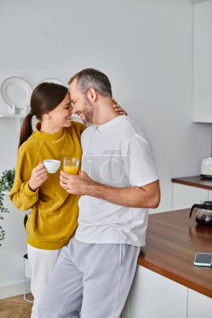 joyful child-free couple with aromatic coffee and fresh orange juice smiling face to face in kitchen