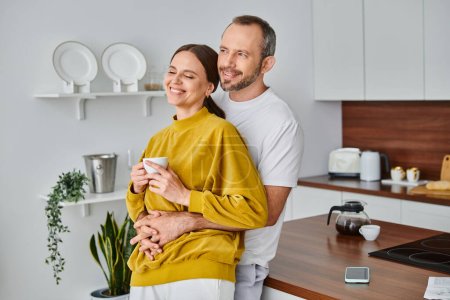 hombre cariñoso abrazando esposa encantada sosteniendo café fresco por la mañana en la cocina, concepto libre de niños
