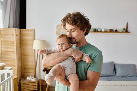 lockige und fröhliche Vater hält seinen kleinen Jungen in einem gemütlichen Schlafzimmer zu Hause, Vaterschaft