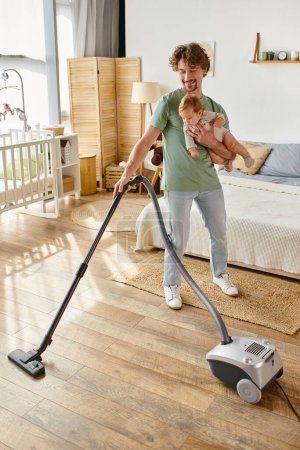 happy father multitasking housework and childcare, man vacuuming bedroom with infant son in arms