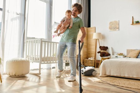 happy man multitasking housework and childcare, father vacuuming hardwood floor with infant in arms