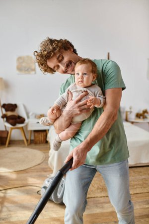 Mann Multitasking Hausarbeit und Kinderbetreuung, glücklicher Vater staubsaugt Hartholzboden mit Baby im Arm