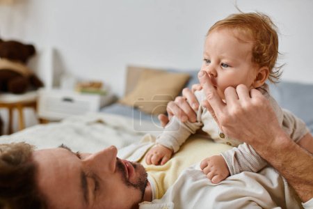 man with curly hair and beard touching nose of his infant son, bond between father and child
